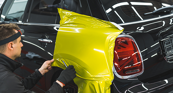 Technician applying a vinyl wrap to a car’s rear side panel.
